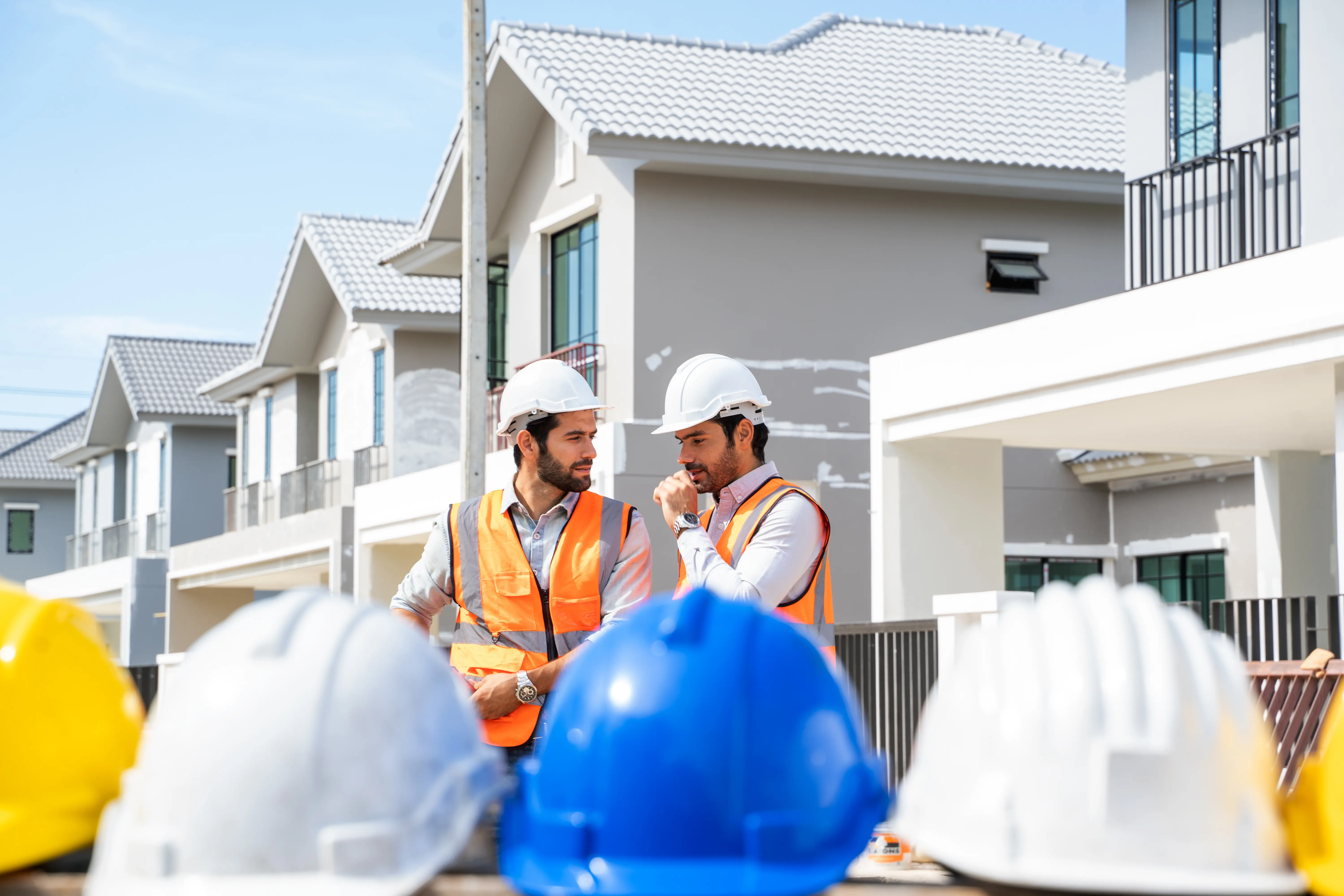 Two construction workers speaking to one another in front of a construction site.